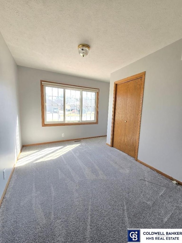 carpeted empty room with baseboards and a textured ceiling