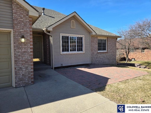 exterior space with a patio, brick siding, and roof with shingles