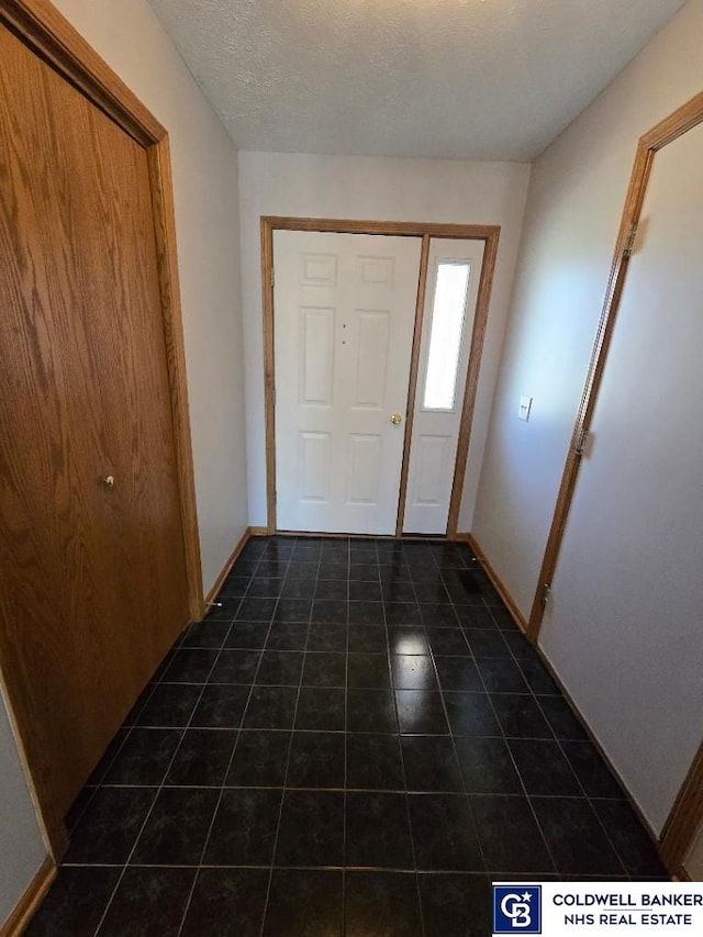 foyer entrance with tile patterned flooring, a textured ceiling, and baseboards