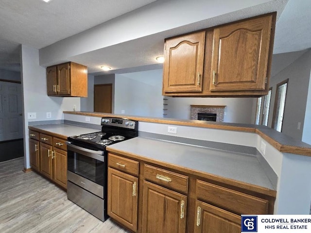 kitchen featuring a fireplace, brown cabinetry, stainless steel electric range, and light wood-type flooring