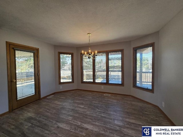 unfurnished dining area featuring a textured ceiling, plenty of natural light, wood finished floors, and a chandelier