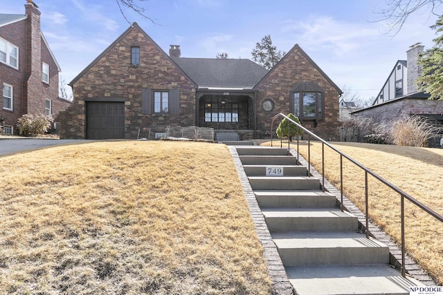 english style home with a front lawn, stairway, an attached garage, brick siding, and a chimney