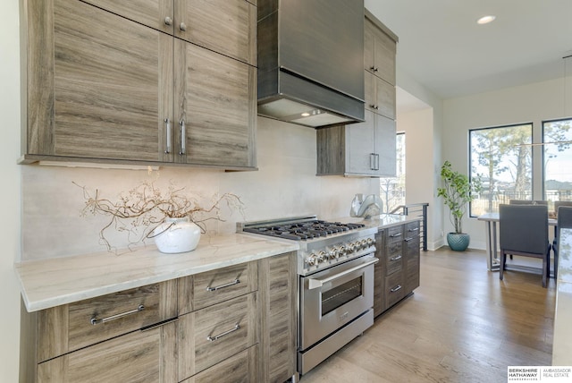 kitchen with baseboards, custom range hood, light stone counters, light wood-style flooring, and stainless steel stove