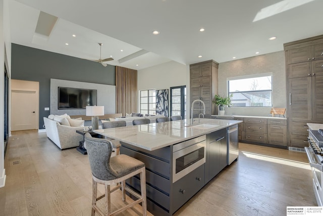 kitchen featuring a center island with sink, a sink, appliances with stainless steel finishes, a breakfast bar area, and light wood finished floors