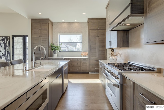 kitchen with light wood finished floors, light stone countertops, custom exhaust hood, stainless steel appliances, and a sink