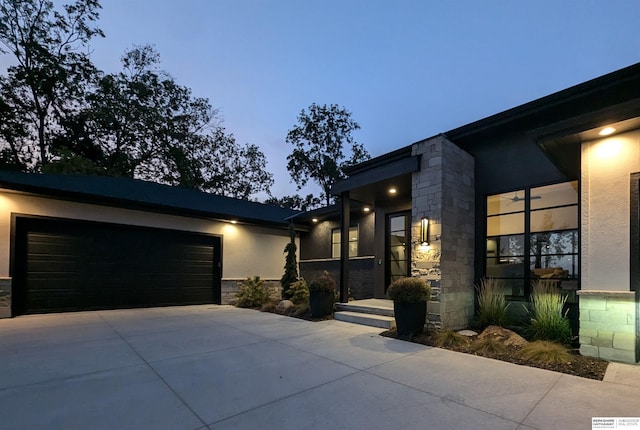 contemporary home with stone siding, stucco siding, an attached garage, and concrete driveway