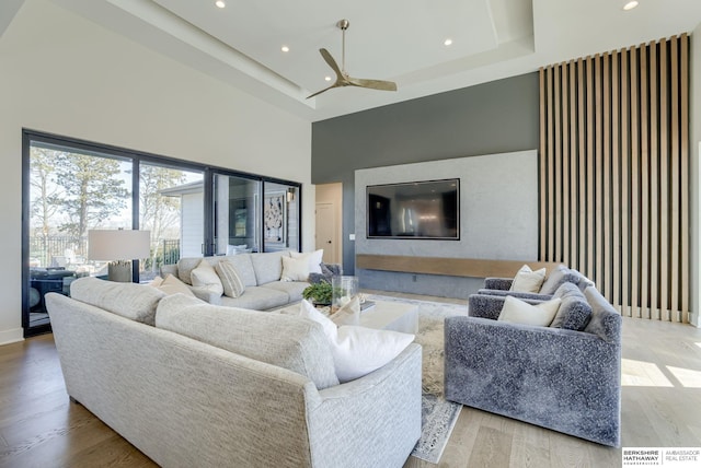 living room with recessed lighting, light wood-style flooring, a raised ceiling, and a towering ceiling