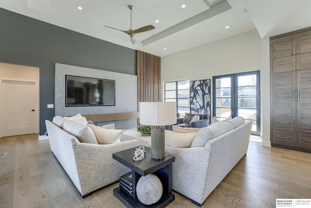 living room with recessed lighting, light wood-style flooring, a raised ceiling, and a towering ceiling