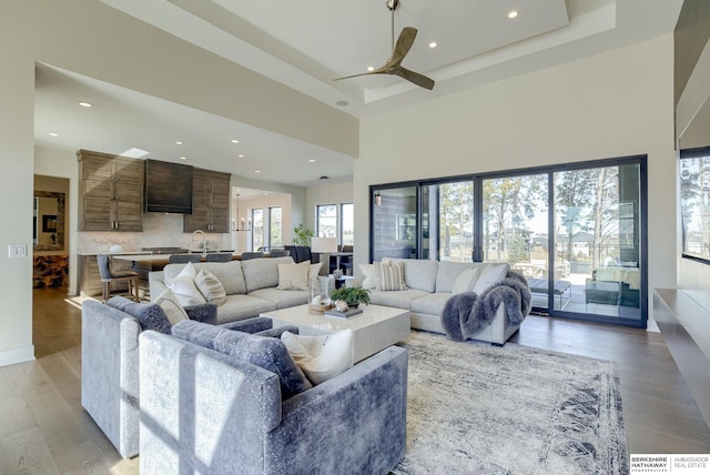 living room with recessed lighting, a high ceiling, a tray ceiling, and light wood-style floors