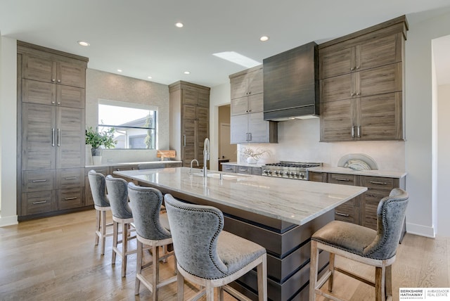 kitchen with a breakfast bar area, premium range hood, light wood-style flooring, a sink, and stainless steel gas stovetop