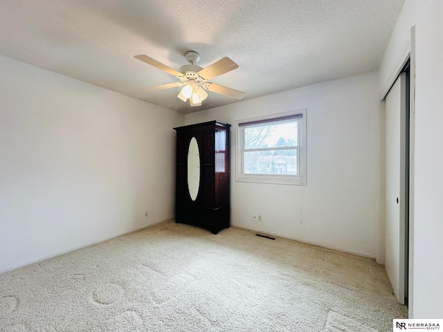 unfurnished bedroom featuring a ceiling fan, visible vents, a closet, a textured ceiling, and carpet flooring