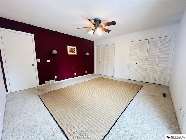 interior space with a ceiling fan, carpet, visible vents, and multiple closets