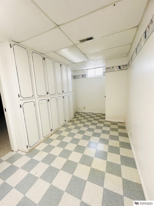 basement with visible vents, baseboards, and a drop ceiling