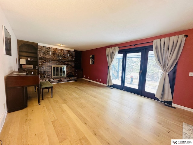 living room with visible vents, baseboards, a brick fireplace, and wood finished floors