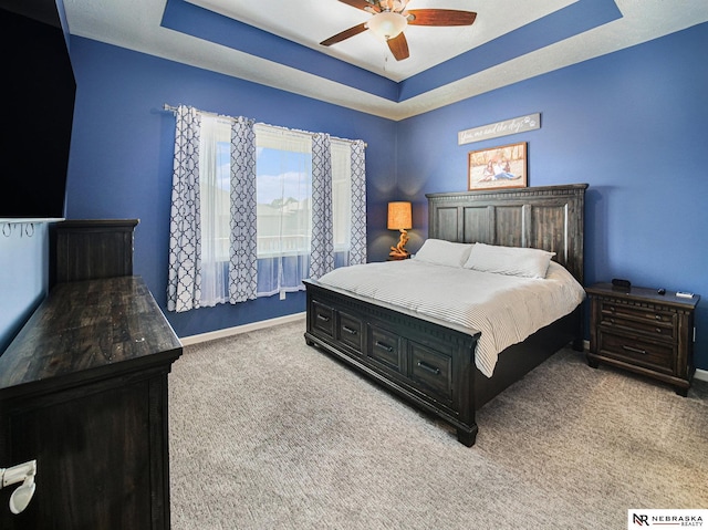 bedroom with a ceiling fan, a tray ceiling, light colored carpet, and baseboards