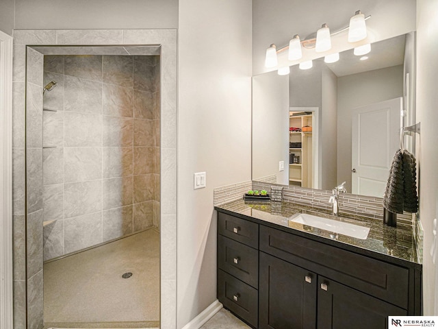 bathroom featuring baseboards, a spacious closet, vanity, and a tile shower