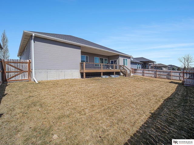 back of house featuring a yard, a deck, a fenced backyard, and a gate