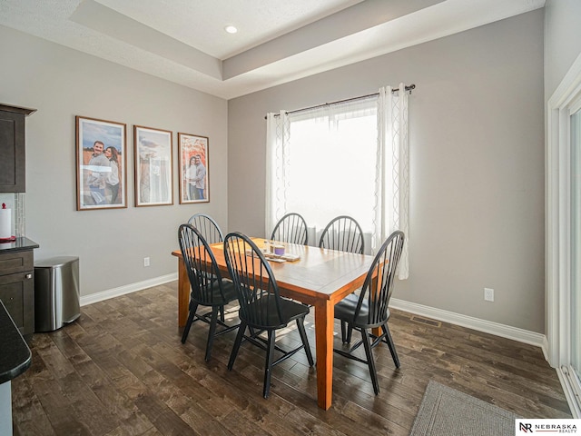 dining space with dark wood finished floors, visible vents, a raised ceiling, and baseboards