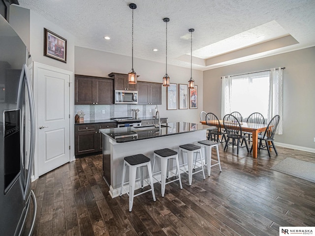 kitchen with dark countertops, a breakfast bar, appliances with stainless steel finishes, a raised ceiling, and a sink