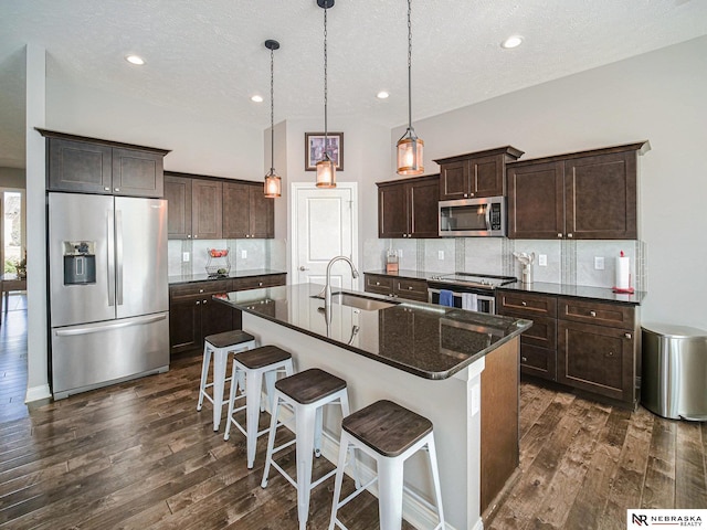 kitchen with a sink, backsplash, appliances with stainless steel finishes, and dark wood-style flooring