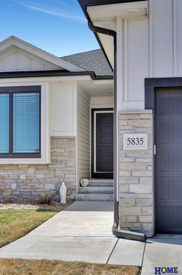 entrance to property with board and batten siding, stone siding, and roof with shingles