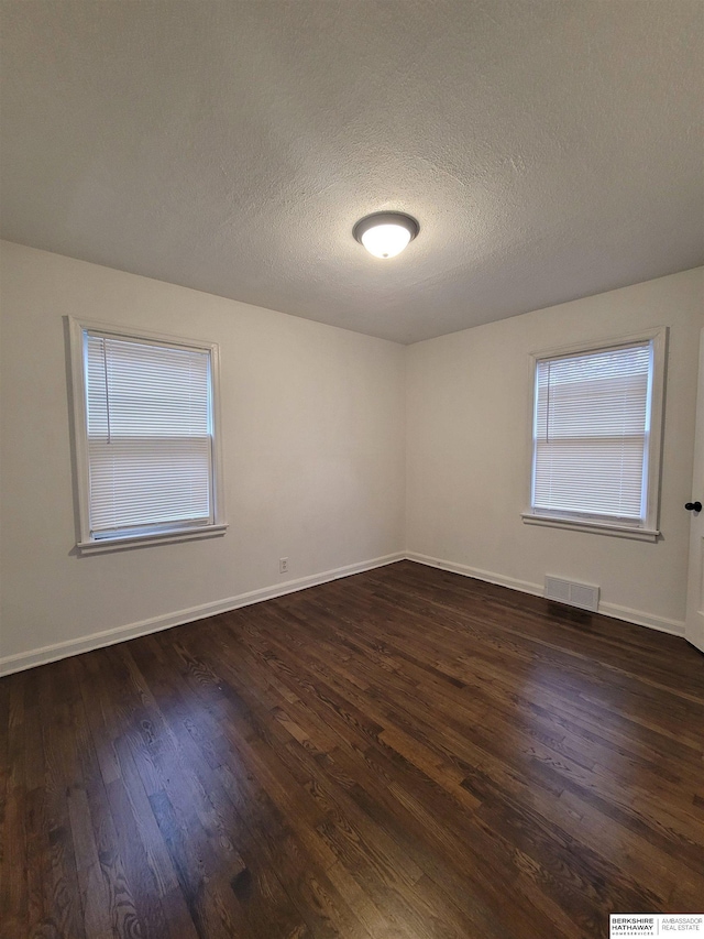 spare room featuring dark wood-type flooring, baseboards, visible vents, and a textured ceiling