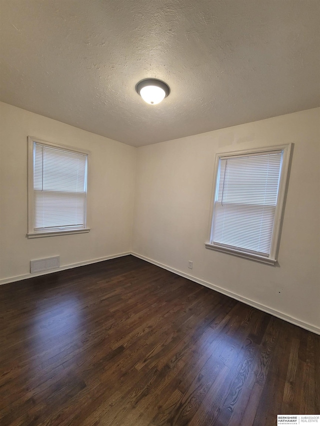 empty room with visible vents, baseboards, a textured ceiling, and dark wood finished floors