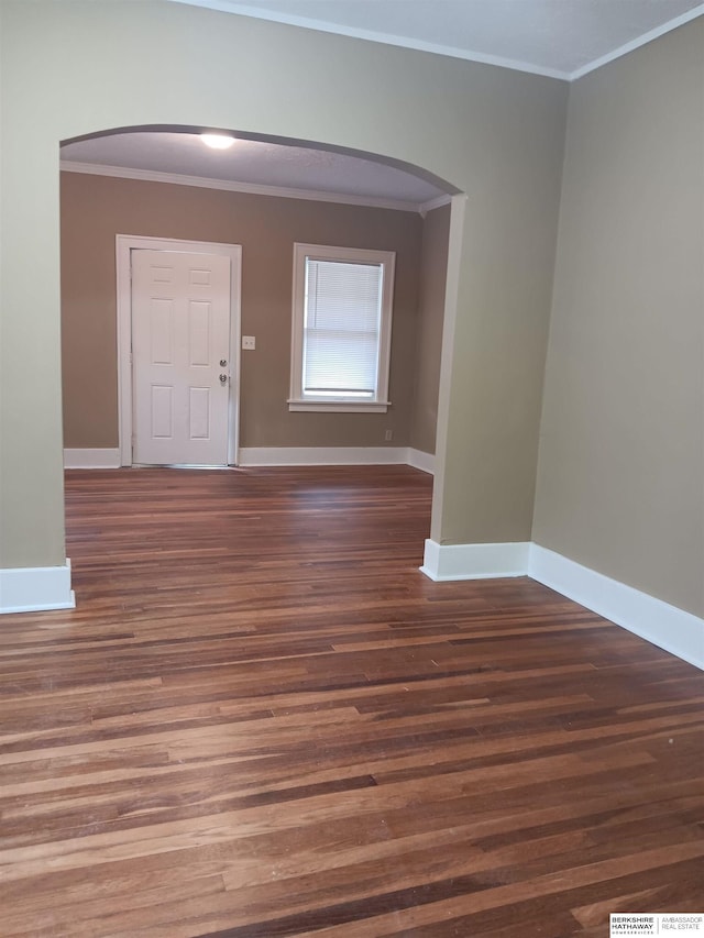 spare room with arched walkways, crown molding, baseboards, and wood finished floors