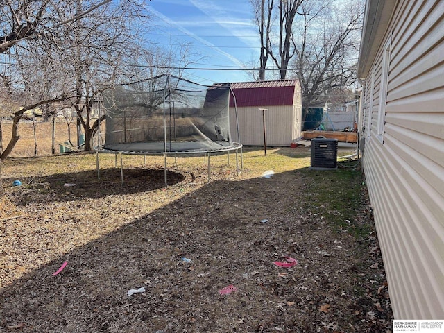 view of yard featuring a trampoline, central AC, fence, a storage shed, and an outdoor structure