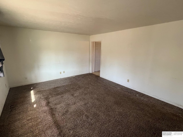 spare room with dark carpet and baseboards