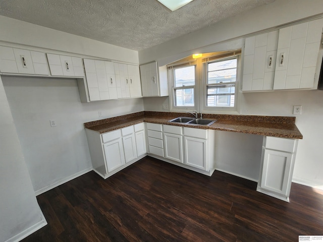 kitchen featuring dark countertops, white cabinets, dark wood-style floors, and a sink