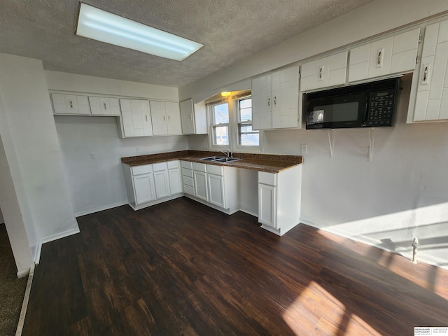 kitchen with dark wood-type flooring, a sink, dark countertops, a textured ceiling, and black microwave