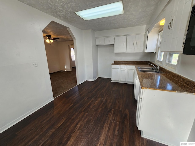 kitchen featuring arched walkways, a sink, white cabinets, a textured ceiling, and dark countertops