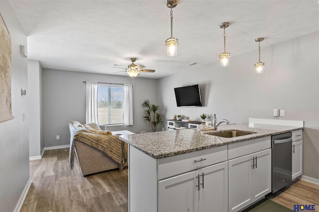 kitchen featuring light wood finished floors, open floor plan, dishwasher, a peninsula, and a sink