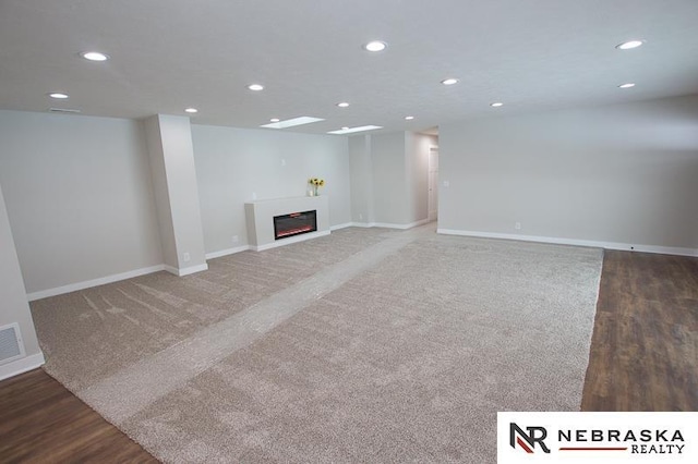 unfurnished living room with a glass covered fireplace, wood finished floors, recessed lighting, and baseboards