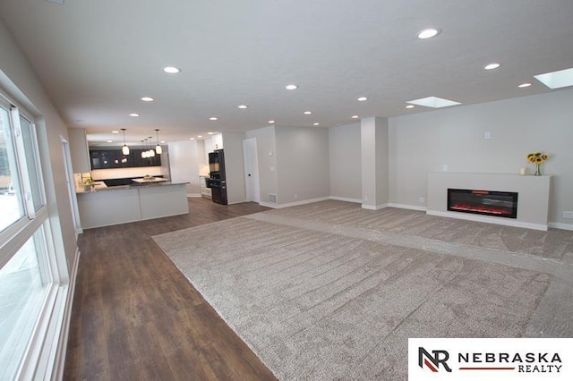 unfurnished living room featuring a glass covered fireplace, wood finished floors, recessed lighting, and baseboards