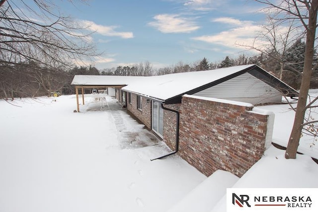 view of snowy exterior featuring brick siding