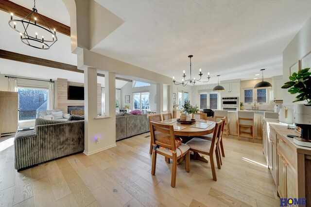 dining room featuring beamed ceiling, a notable chandelier, a fireplace, and light wood-type flooring