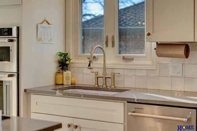 kitchen with tasteful backsplash, white cabinets, stainless steel appliances, and a sink