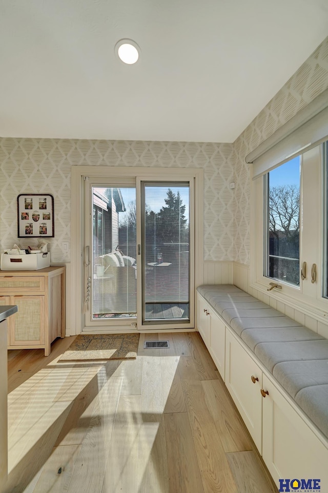 interior space with wallpapered walls, light wood-style floors, and visible vents