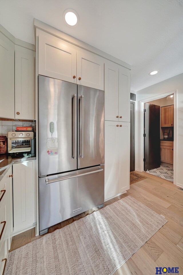 kitchen featuring tasteful backsplash, dark countertops, light wood-style flooring, high quality fridge, and white cabinetry