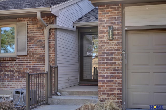 entrance to property featuring brick siding, a garage, central air condition unit, and roof with shingles