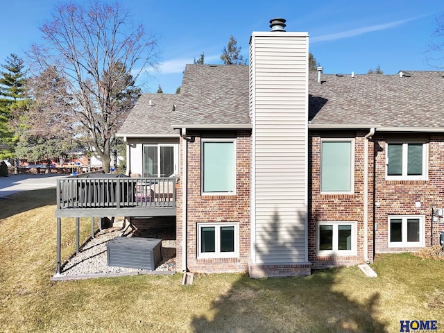 rear view of house with brick siding, a wooden deck, roof with shingles, a chimney, and a yard