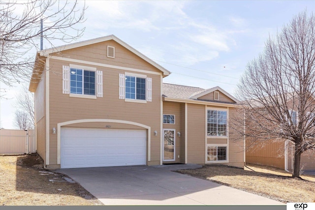 split level home with concrete driveway, a garage, and fence