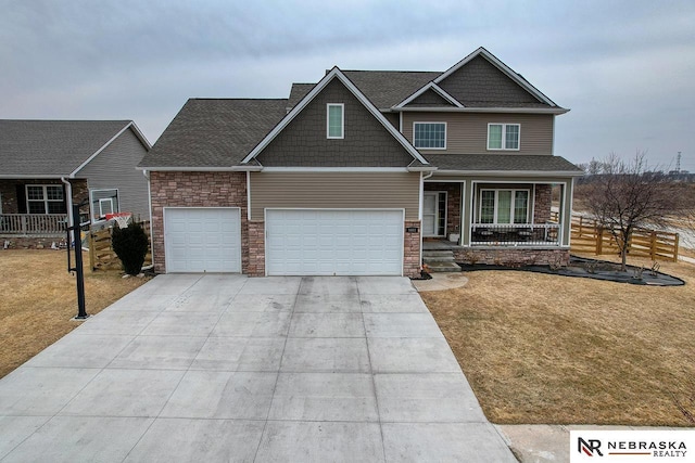 craftsman-style house featuring driveway, stone siding, a porch, fence, and a front yard