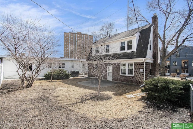 rear view of house with brick siding, fence, a gambrel roof, roof with shingles, and a patio area