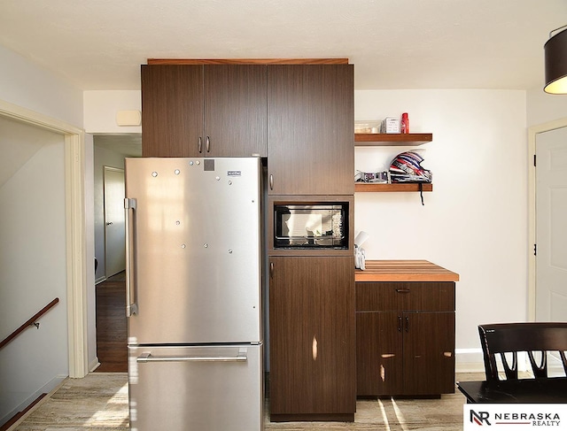 kitchen with open shelves, freestanding refrigerator, dark brown cabinetry, black microwave, and light wood finished floors