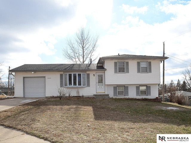 tri-level home with entry steps, concrete driveway, an attached garage, and a front lawn