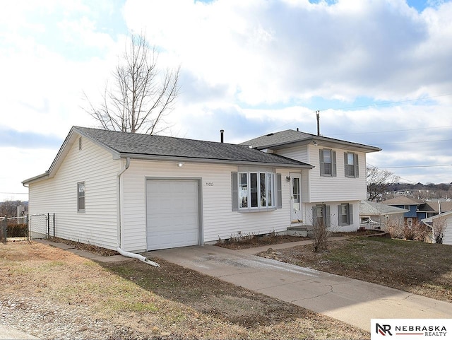 tri-level home featuring driveway, a shingled roof, a garage, and fence