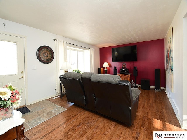 living room featuring an accent wall, baseboards, and wood finished floors